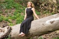 Blonde, young and beautiful woman dressed in black and sitting on the trunk of a fallen eucalyptus tree in the forest, the woman Royalty Free Stock Photo