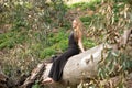 Blonde, young and beautiful woman dressed in black and sitting on the trunk of a fallen eucalyptus tree in the forest, the woman Royalty Free Stock Photo