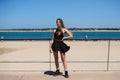 Blonde, young and beautiful woman dressed in black skirt and black top is on the promenade of the sea. The girl is doing different Royalty Free Stock Photo