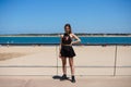 Blonde, young and beautiful woman dressed in black skirt and black top is on the promenade of the sea. The girl is doing different Royalty Free Stock Photo