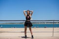 Blonde, young and beautiful woman dressed in black skirt and black top is on the promenade of the sea. The girl puts her hands Royalty Free Stock Photo