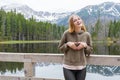 Blonde young girl holding hands in heart shape by the mountain lake in the woods. Travel and active life concept Royalty Free Stock Photo