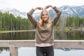 Blonde young girl holding hands in heart shape by the mountain lake in the woods. Travel and active life concept Royalty Free Stock Photo