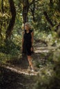 Blonde young women in a black dress with a hood walks in a mysterious forest Royalty Free Stock Photo