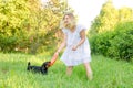 A blonde young woman in a light dress is holding a flying disc that a cute dog clung to