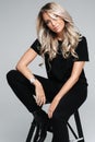 Blonde young woman looking at camera, smiling, wear black t-shirt, posing sitting on chair. Studio. Royalty Free Stock Photo