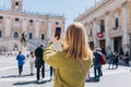 Blonde young Woman with smartphone is walking on a sunny day. Capitol in Rome, Piazza del Campidoglio in Capitoline Hill Royalty Free Stock Photo