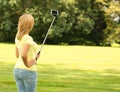 Blonde young woman taking selfie photo with stick in park Royalty Free Stock Photo