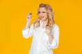 Blondine woman in white shirt, middle aged European girl winking and smiling broadly while holding mascara and applying it while Royalty Free Stock Photo