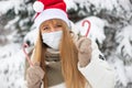 Blondy girl in medical mask , red Santa hat and sweets, in the winter park