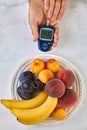 A blood glucose meter in the hands of a man and a plate of fruit
