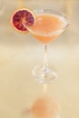 Blood orange alcohol beverage in a glass on a reflective surface