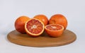 The blood orange cut in half with bright juicy pulp against a background of three whole oranges on a round wooden tray against Royalty Free Stock Photo