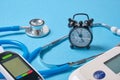 Blood pressure monitor, glucometer, stethoscope, notepad and alarm clock on blue background