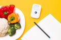 blood pressure monitor on a yellow background, a notebook and a white large plate with vegetables