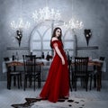 Bloodthirsty female vampire in red dress. Medieval interior