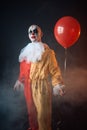 Bloody clown in carnival costume holds air balloon