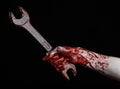 Bloody hand holding a big wrench, bloody wrench, big key, bloody theme, halloween theme, crazy mechanic, black background Royalty Free Stock Photo