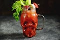 Bloody Mary cocktail in glass skull with celery sticks, pink salt, lime and canapes from canned vegetables. Halloween drink. Royalty Free Stock Photo