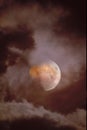 Bloody moon close-up when eclipsed against a background of clouds through which breaks light from the moon, view through the teles