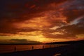 Bloody sky above bridge and reflective water surface waves. Red cloudy sunset above lake at dusk. Evening cloudscape in twilight. Royalty Free Stock Photo