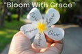 Inspirational quote - Bloom with Grace. With positive words on white Bali flower in hand on green enviroment background.