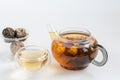 Blooming black tea in a glass teapot. On a light surface. Nearby are tea briquettes of leaves and flowers. In the background is a Royalty Free Stock Photo