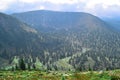 blooming grass meadow with flowers among trees in green Baikal mountain .ridge in shadows of clouds, blue sky, river Royalty Free Stock Photo