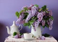 Blooming purple lilac in a jug, Cup and teapot. Still life in ru