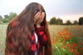 Blooming red poppies in summer field, girl with long hair stands, covering her face with her hands and crying, concept of