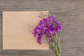 Blooming sally purple flowers with craft paper blank on old grunge wooden background. Top view. Minimalistic mockup. Royalty Free Stock Photo