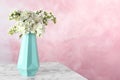 Blossoming lilac flowers in vase on marble table against color background