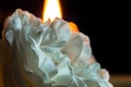 A blossoming rose flower with white petals, on a black background and a candle burning behind. Macro