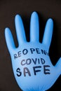 Blown up blue latex surgical glove on black background. Reopening covid safe. Open again text written on medical glove. New normal
