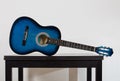 Blue acoustic guitar on a black wooden table isolated on grey wall background. Trendy musical instrument for playing good music.