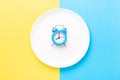 Blue alarm clock and empty plate on colored paper background. Intermittent fasting concept Royalty Free Stock Photo