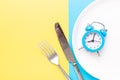 Blue alarm clock, fork, knife and empty plate on colored paper background. Intermittent fasting concept Royalty Free Stock Photo