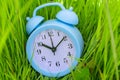 Blue alarm clock lying on bright lush young green grass. Metaphor