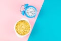 Blue alarm clock with oatmeal on a pink and blue background. Healthy nutrition concept. Top views with clear space