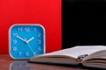 Blue alarm clock and opened personal organizer on red and black background