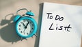 Blue alarm clock beside to-do list on beige surface reflecting time management Royalty Free Stock Photo