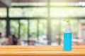 Blue alcohol gel in pump clear bottle put on wooden table with blurry image of coffee shop or cafe restaurant in background.