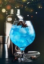 Blue alcoholic cocktail with sambuca, liqueur, lemon juice, crushed ice and anise stars in big wine glass with bartender steel
