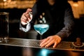 Blue alcoholic cocktail in wineglass stands on bar counter. Bartender`s hand near glass.