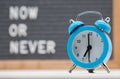 blue analog alarm clock on English text background now or never Royalty Free Stock Photo