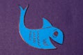 Blue april fool fish cut out of colored paper on a purple background