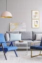 Blue armchair near white table and grey sofa in modern living room interior with poster. Real photo Royalty Free Stock Photo