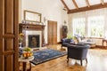 Blue armchairs and patterned carpet in front of wooden fireplace in sophisticated interior. Real photo