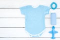 Blue baby clothes for little boy. Bodysuit, toys, cosmetics on white wooden background top view copy space