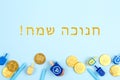 Blue background with multicolor dreidels, menora candles and chocolate coins with Happy Hanukkah wording in Hebrew Royalty Free Stock Photo
